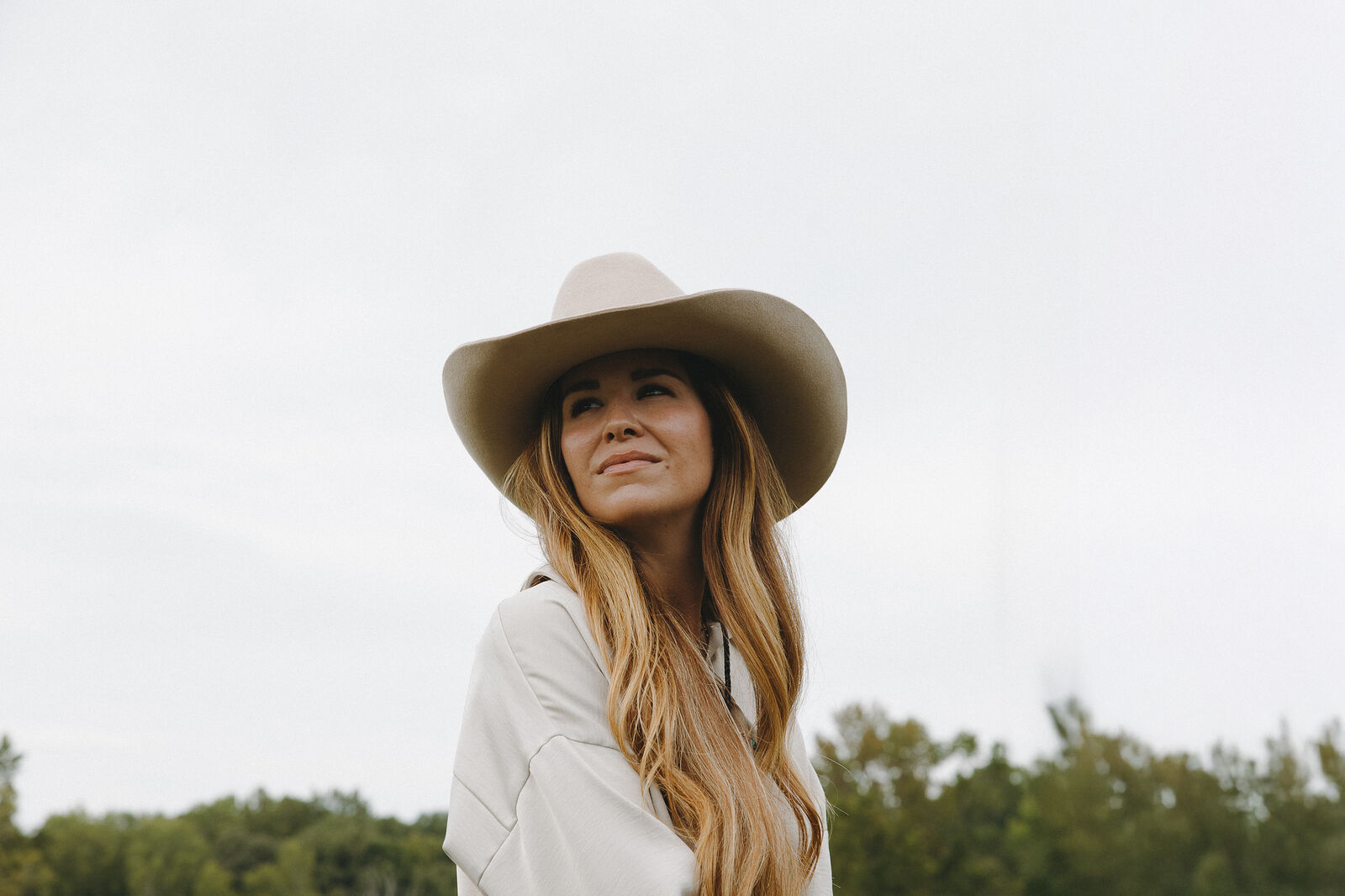 Woman in a cream hat smiling toward the sky